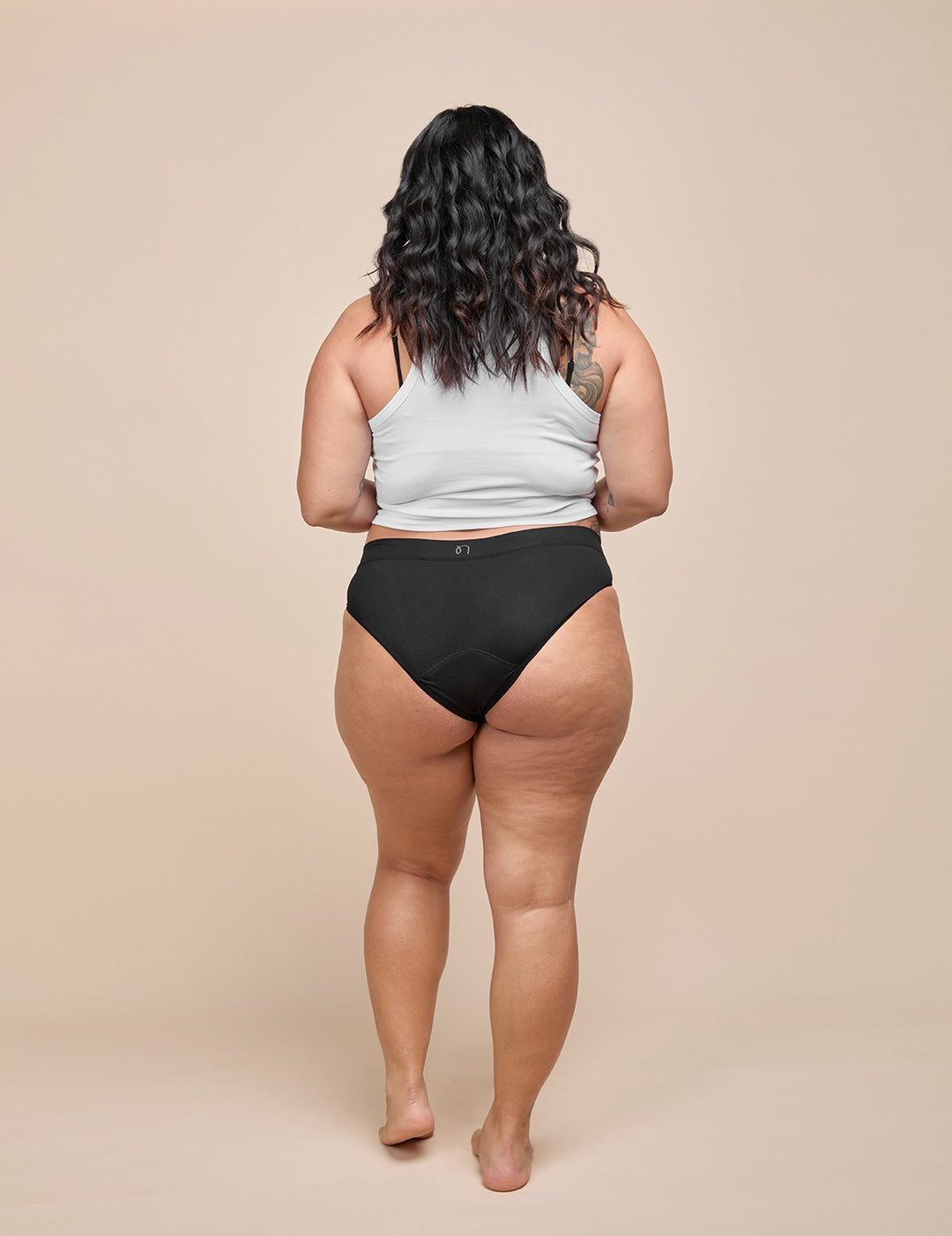Model wearing the black moderate absorbency bikini with a white tank top, back view