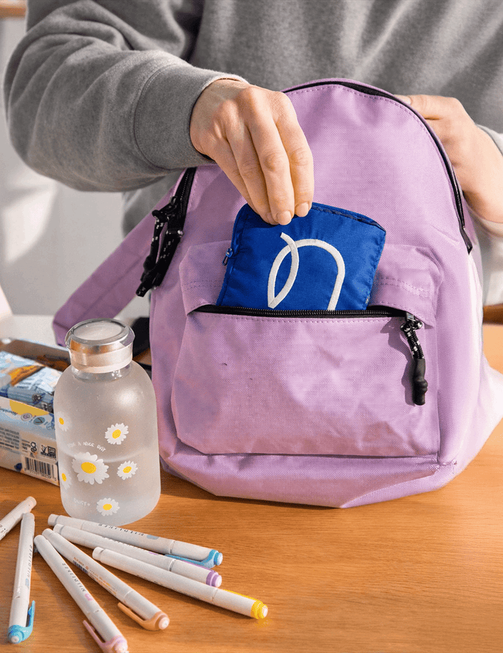 Reusable pouch next to a lilac backpack, small enough to fit in your bag